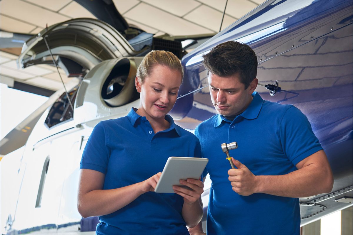 Maintenance personnel reviewing work on a tablet beside an aircraft